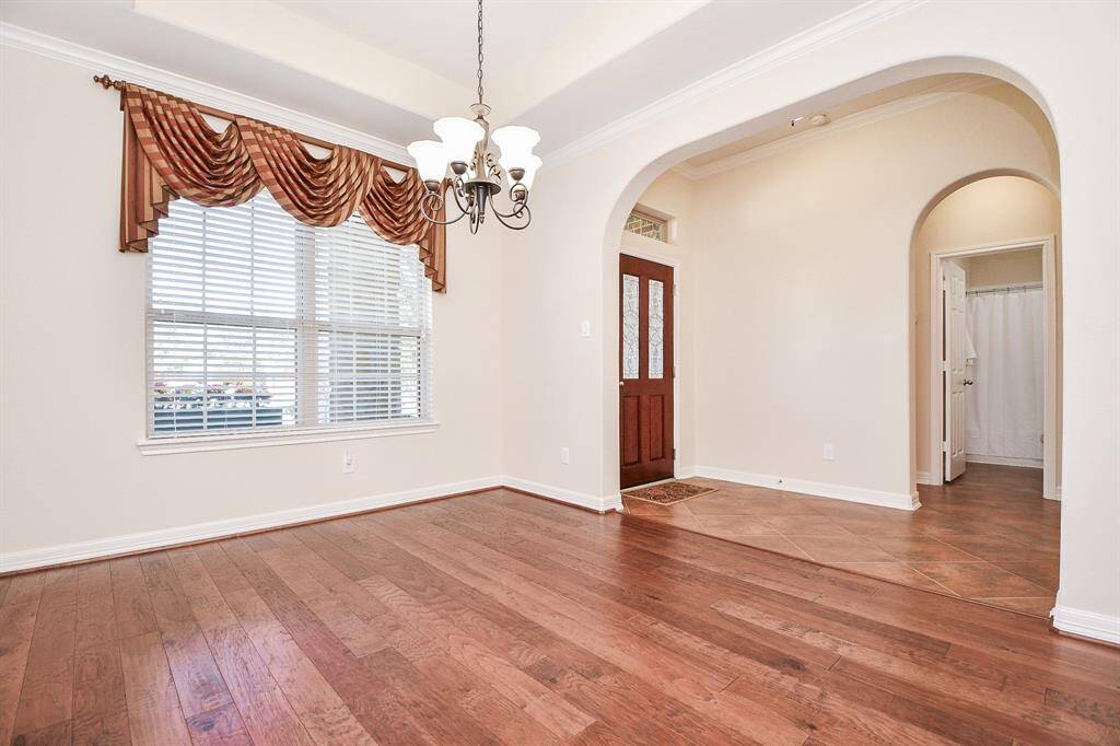 This photo showcases a bright entryway with rich wood flooring and a welcoming arched doorway. A large window with elegant drapes allows natural light to flood in, highlighting the classic chandelier and warm, neutral walls. The space offers a seamless flow into adjoining rooms, ideal for creating an inviting atmosphere.