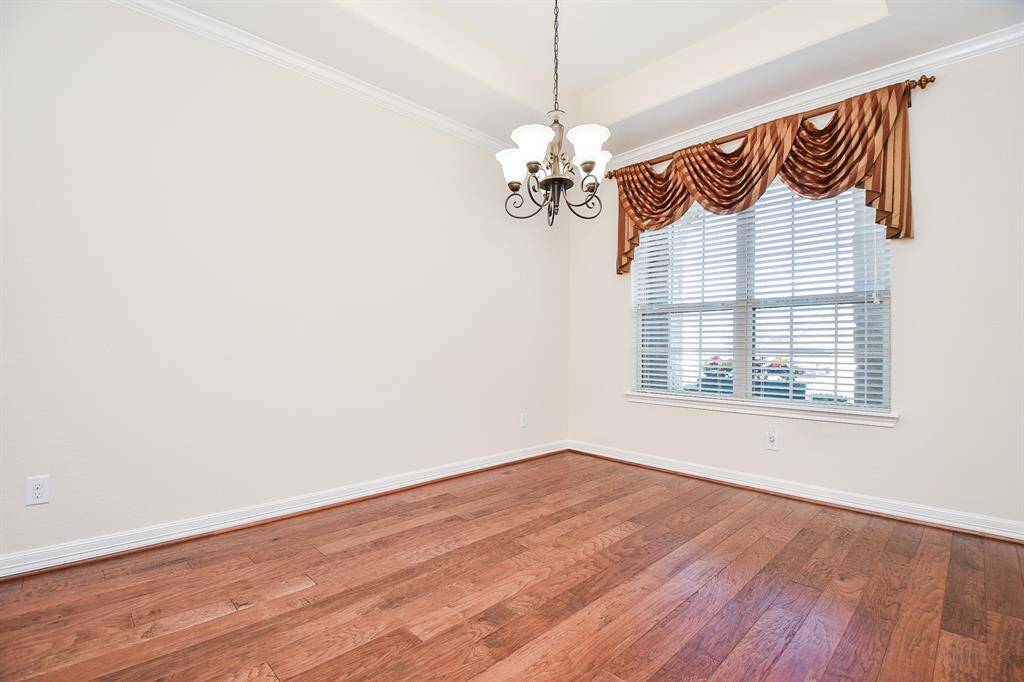 This dining room features hardwood floors, a decorative chandelier, and a large window with elegant drapery, providing plenty of natural light.