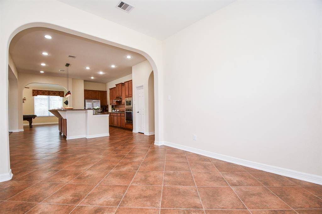 This photo showcases a spacious open-concept kitchen and living area with tiled flooring, recessed lighting, and warm wooden cabinetry. The kitchen features a large island and ample counter space, ideal for cooking and entertaining. Arched entryways add an elegant touch.