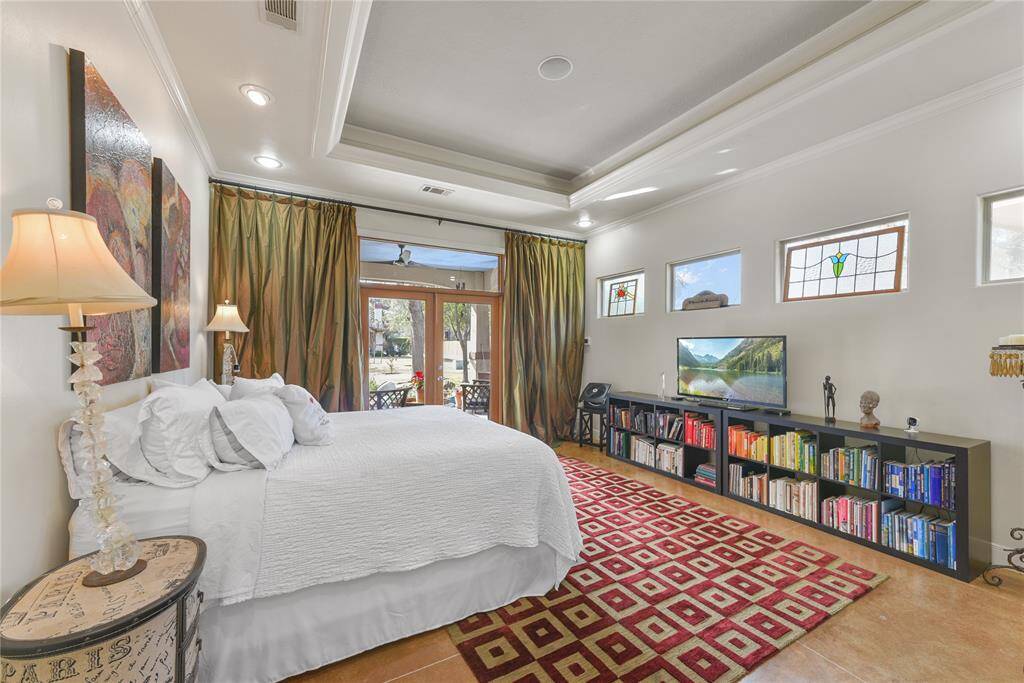 Here is the very comfortable Primary bedroom in the rear house!  The high ceilings even with the extra tray ceiling treatment give it an air of spaciousness..  There is still plenty of natural light and French doors out to the front patio viewing the beautiful yard, pool, and plantings.