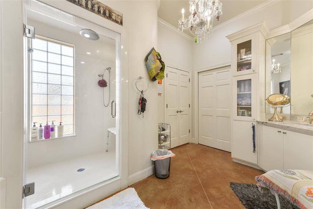 The Primary Bath in the second home is thoughtfully presented in neutral tones throughout.  There is the oversized shower with glass block window to allow for plenty of natural light plus there is a separate water closet, tub, vanity area, and large walk-in closet.  Above, a chandelier adds a bit of sparkle.