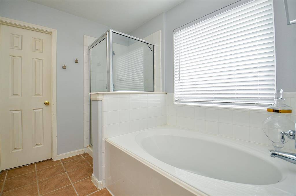 It has a sleek glass-enclosed shower next to a white bathtub.