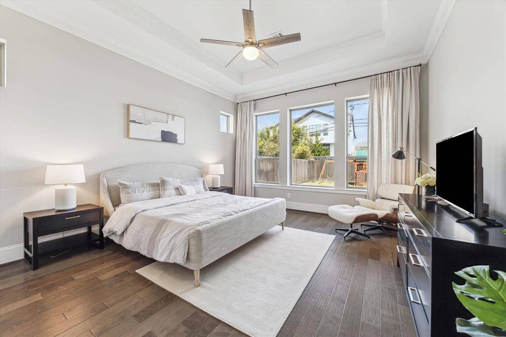 Designed for relaxation, this primary bedroom showcases soaring tray ceilings, hardwood floors, and expansive windows overlooking the backyard. Large windows flood the space with natural light while maintaining privacy. A neutral color palette enhances the airy feel, creating a tranquil retreat. Positioned away from the main living areas, this suite offers the perfect blend of comfort and sophistication.