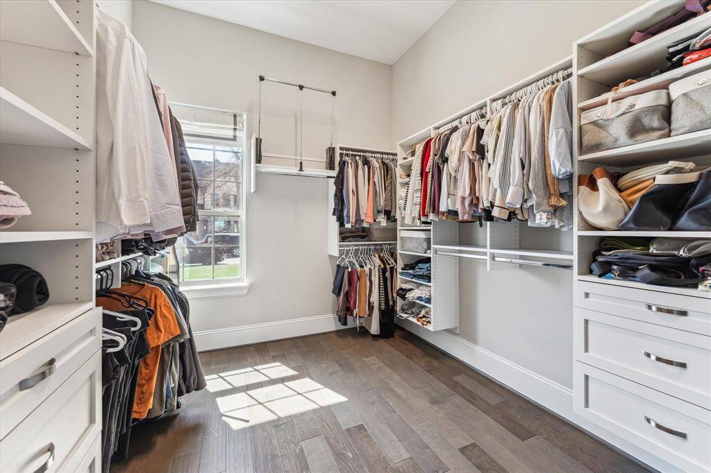 A well-appointed walk-in closet featuring custom built-ins, adjustable shelving, and a mix of hanging space and drawers for effortless organization. A large window brings in natural light, while high ceilings and a pull-down clothing rod maximize vertical storage. The elegant design blends functionality with style, creating a refined dressing space.