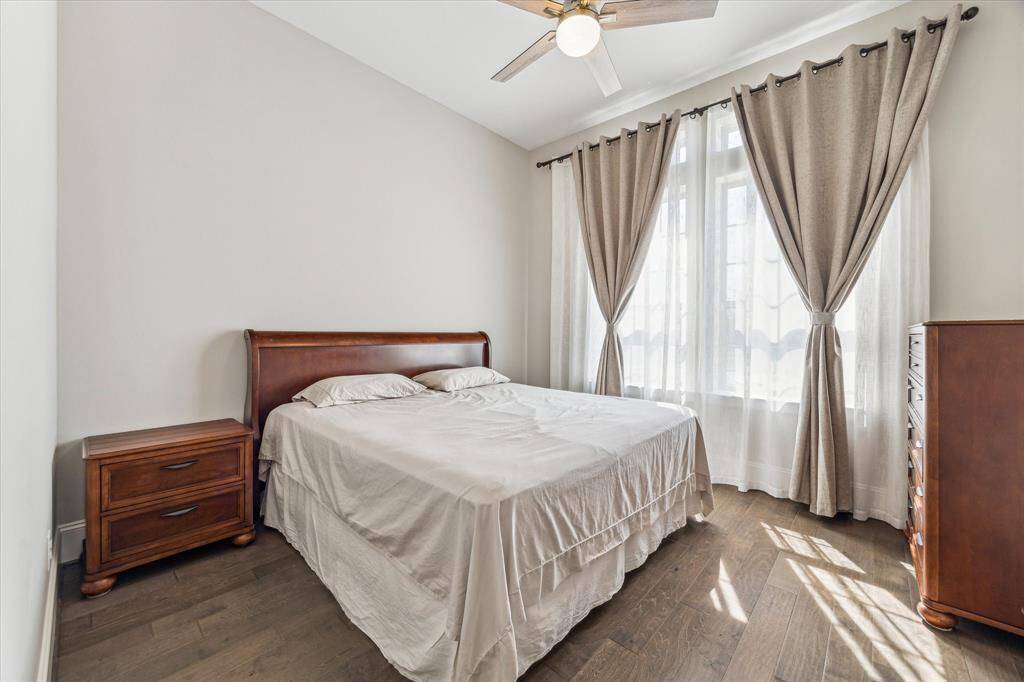This spacious first-floor secondary bedroom features hardwood flooring, tall ceilings, and oversized windows that allow natural light to flow in. A neutral color palette enhances the inviting atmosphere, while the ceiling fan ensures year-round comfort. Ideal as a guest suite, home office, or multi-generational living space, this room offers flexibility and convenience.