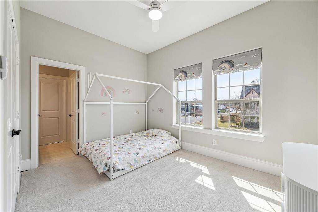 This secondary bedroom offers a light-filled retreat with tall ceilings, oversized windows, and soft carpeting for added comfort. The neutral color scheme provides a versatile backdrop, while the room’s layout allows for flexibility in design and function.