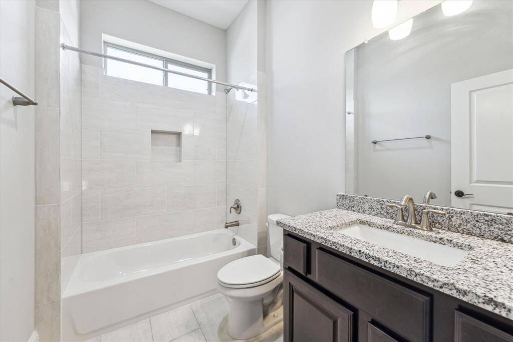 Tiled shower/tub combo includes a built-in niche for convenience, while a high transom window brings in natural light while maintaining privacy. Thoughtfully designed for both style and function, this space is ideal for guests or secondary bedrooms.