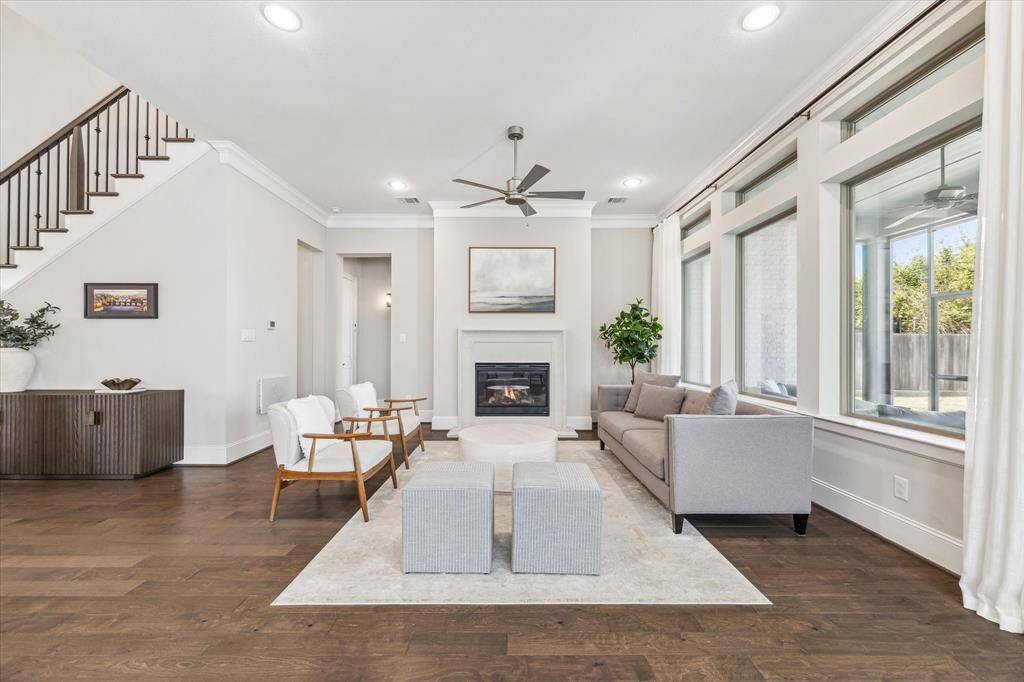 This beautifully designed living room offers a seamless blend of comfort and sophistication. Floor-to-ceiling windows provide abundant natural light and views of the backyard. Crown molding, recessed lighting, and rich hardwood floors enhance the room’s refined aesthetic. Strategically positioned within the open floor plan, this space connects effortlessly to the kitchen and dining areas, making it an ideal setting for gatherings.
