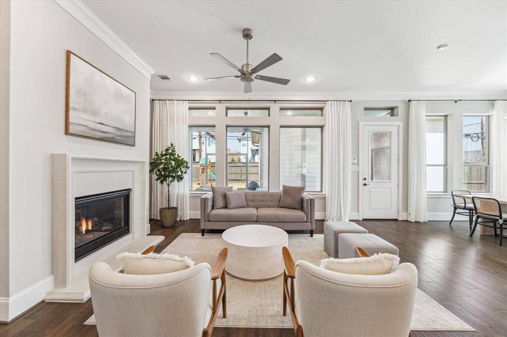 Expansive windows and a glass-paneled door bring in natural light while offering easy access to the backyard. A sleek gas fireplace adds warmth and serves as a focal point, blending seamlessly with the open-concept layout for effortless entertaining.