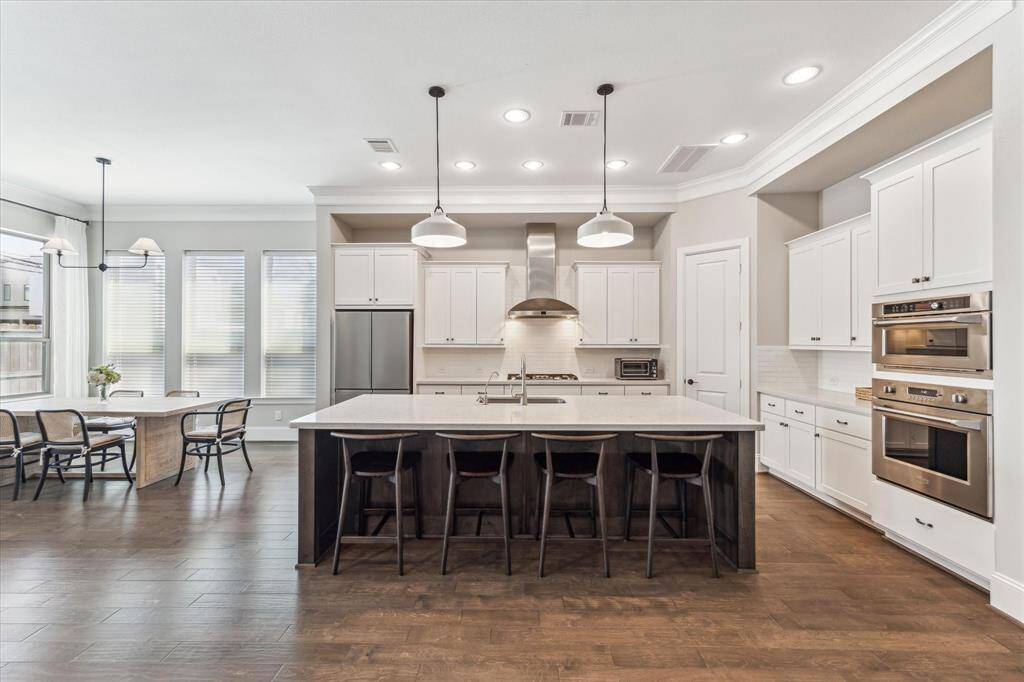 Sophistication meets practicality in this beautifully designed kitchen with an open-concept flow. The oversized island with quartz countertops provides ample workspace and seating, while pendant lighting adds a stylish touch. A gas cooktop with a stainless steel vent hood, built-in double ovens, and custom cabinetry enhance the kitchen’s efficiency. Positioned adjacent to the dining area and living room, this space ensures seamless connection for hosting or casual meals.