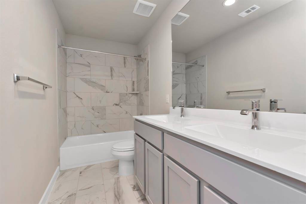 Sophistication within the secondary bathroom, where tile flooring perfectly complements a bath/shower combo surrounded by tile. Light wood cabinets, and double sinks paired with a beautiful light countertop elevate the space, creating a truly inviting ambiance. Sample photo of completed home with similar floor plan. Actual colors and selections may vary.