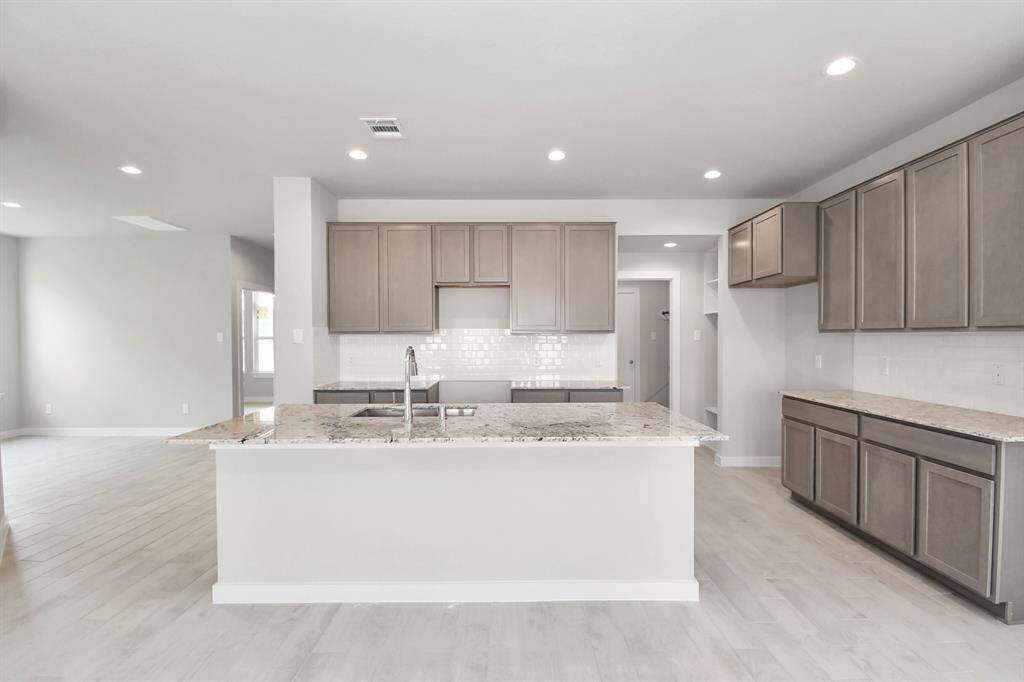 A massive granite island takes center stage, complemented by high ceilings, soft-close cabinets, granite countertops, stainless steel appliances, a sleek tile backsplash, and recessed lighting. The extended counter area adds practicality to the stylish design. The open concept effortlessly connects the kitchen to the expansive family room, forming a perfect hub for gatherings. Sample photo of completed home with similar floor plan. Actual colors and selections may vary.
