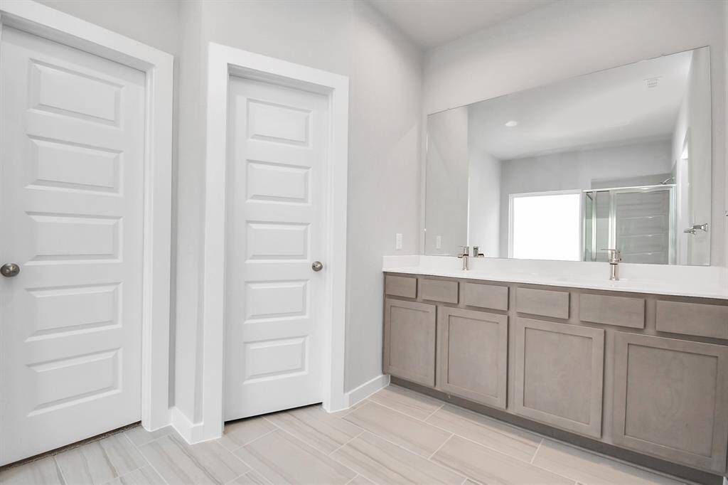 Escape to a spa-like oasis in this primary bathroom. Enjoy a walk-in shower with tile surround, a separate garden tub with custom detailing, and an elegant vanity featuring light countertops, modern hardware, and beautiful vanity lights. Experience luxury and relaxation in every detail. Sample photo of completed home with similar floor plan. Actual colors and selections may vary.