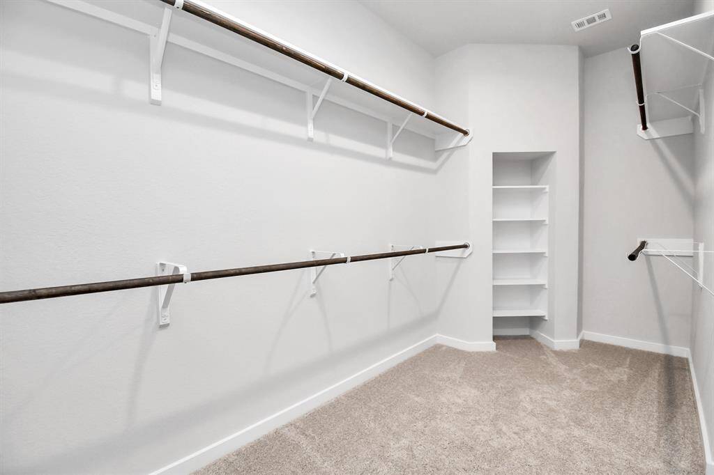 Experience luxury in this spacious walk-in closet with high ceilings and plush carpet. Warm paint tones, built-in shelving, and dark finishes create a contemporary and functional retreat. Sample photo of completed home with similar floor plan. Actual colors and selections may vary.
