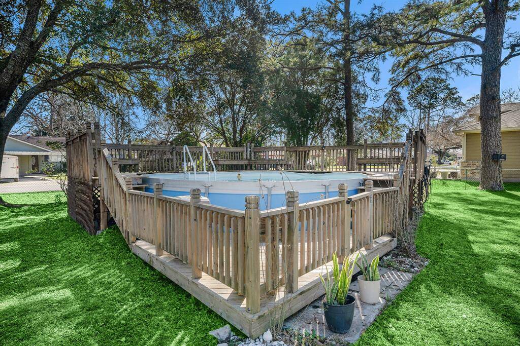 The above-ground pool is surrounded by a wooden deck. The area is shaded by mature trees, offering a relaxing outdoor space ideal for leisure and entertainment.