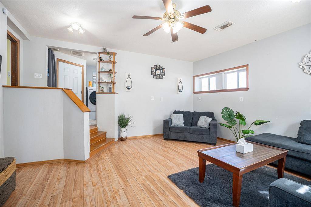 This living room features a cozy layout with light wood flooring and neutral walls. There's a small staircase leading to another area, adding architectural interest. Natural light streams in through narrow windows, enhancing the inviting atmosphere.