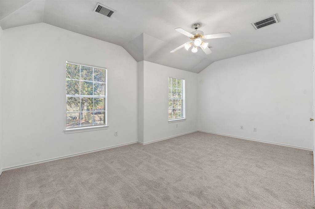 The upstairs primary bedroom features neutral carpet, vaulted ceilings, and two large windows, providing ample natural light. There's also a ceiling fan for added comfort.
