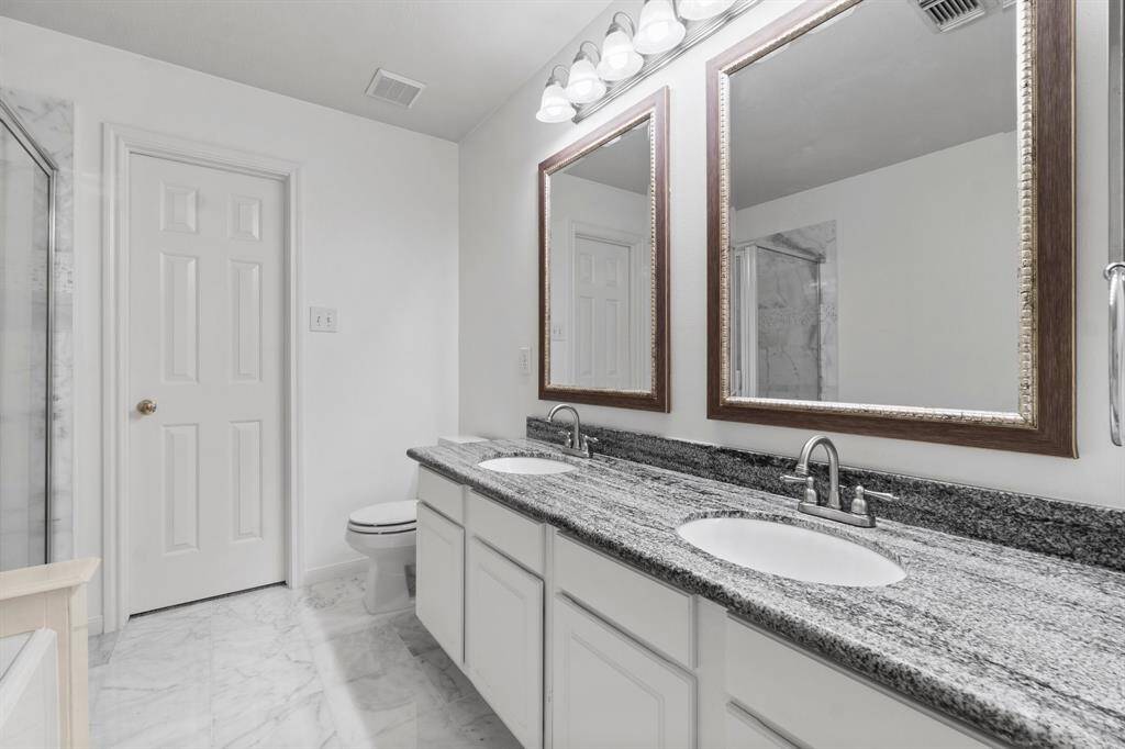The primary bathroom features dual sinks with granite countertops, framed mirrors, and ample cabinetry. It has a neutral color palette with marble flooring.