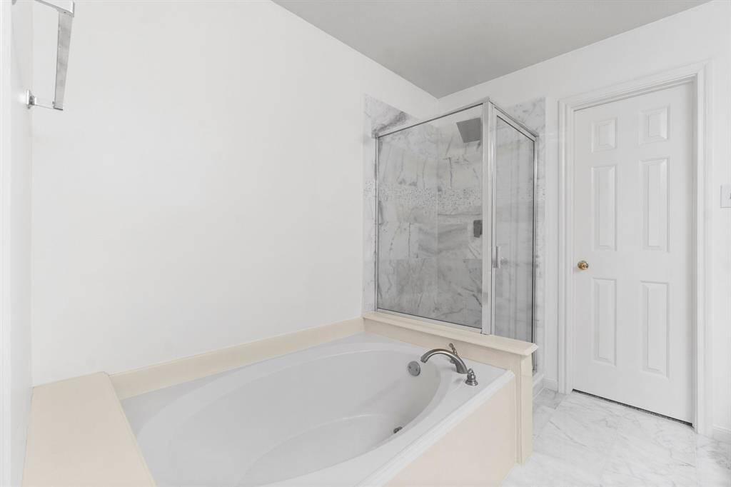 This bathroom features a spacious soaking tub and a separate glass-enclosed shower with a marble tiles, providing a clean and modern look. The room is bright with neutral tones, enhancing the sense of space.