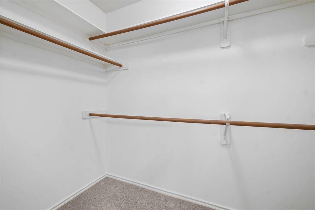 Primary bedroom has spacious walk-in closet with multiple wooden hanging rods and clean, white walls, perfect for ample storage and organization.