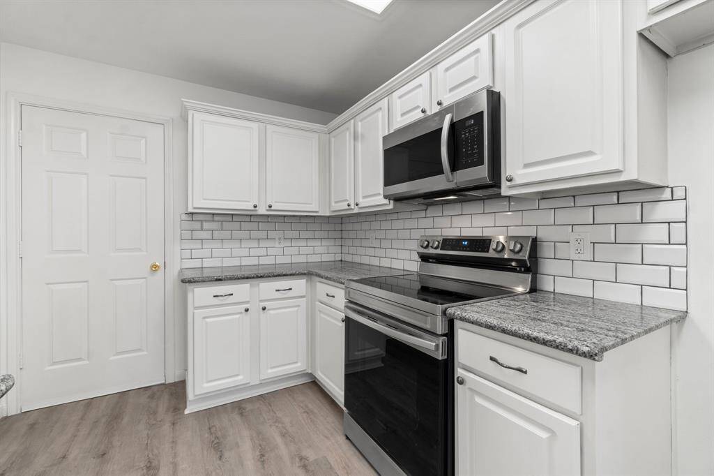 Modern kitchen with white cabinetry and subway tile backsplash. Features new stainless steel appliances, including an oven and microwave, and granite countertops. Light wood flooring complements the bright, clean look.