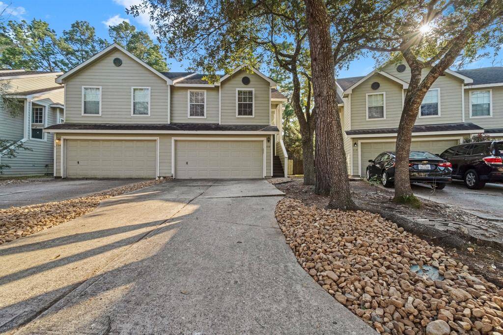 The exterior features a light facade and is surrounded by mature trees, providing shade and a natural setting. The driveway is lined with decorative rocks, enhancing the property's curb appeal.