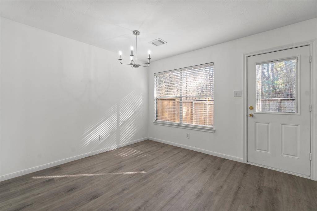 This bright breakfast room has a stylish chandelier, large windows with blinds for natural light, and a door leading outside, creating an inviting space.
