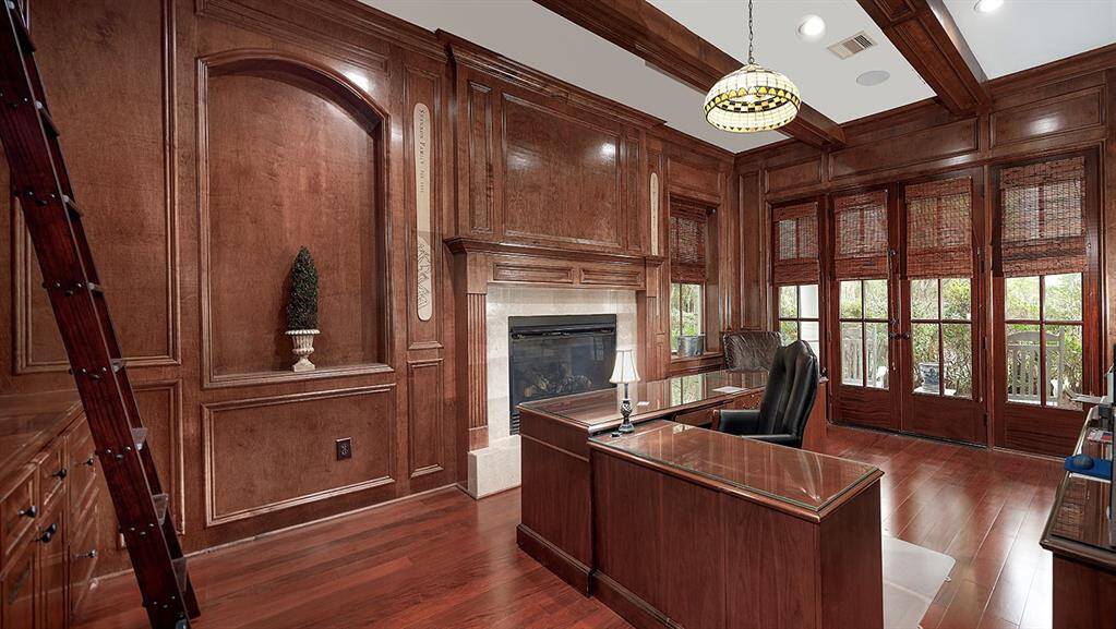 The wood paneled study features a cozy fireplace, library ladder and wood beam ceiling