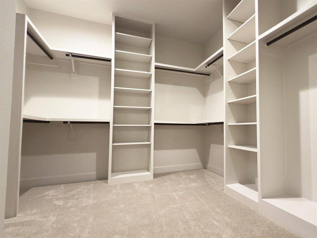 Step into the ROClake's primary bedroom closet, where elegance meets practicality. This expansive space features sleek, built-in shelving and ample hanging space, designed to keep your wardrobe organized and easily accessible. Image depicts home as-is.