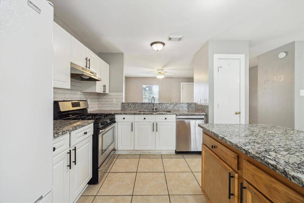 This updated island eat-in kitchen features granite countertops, tile backsplash, a stainless steel range, hood vent, and dishwasher, crisp white cabinetry with modern pulls, a large pantry and in-kitchen utility area tucked discreetly behind bi-fold doors.