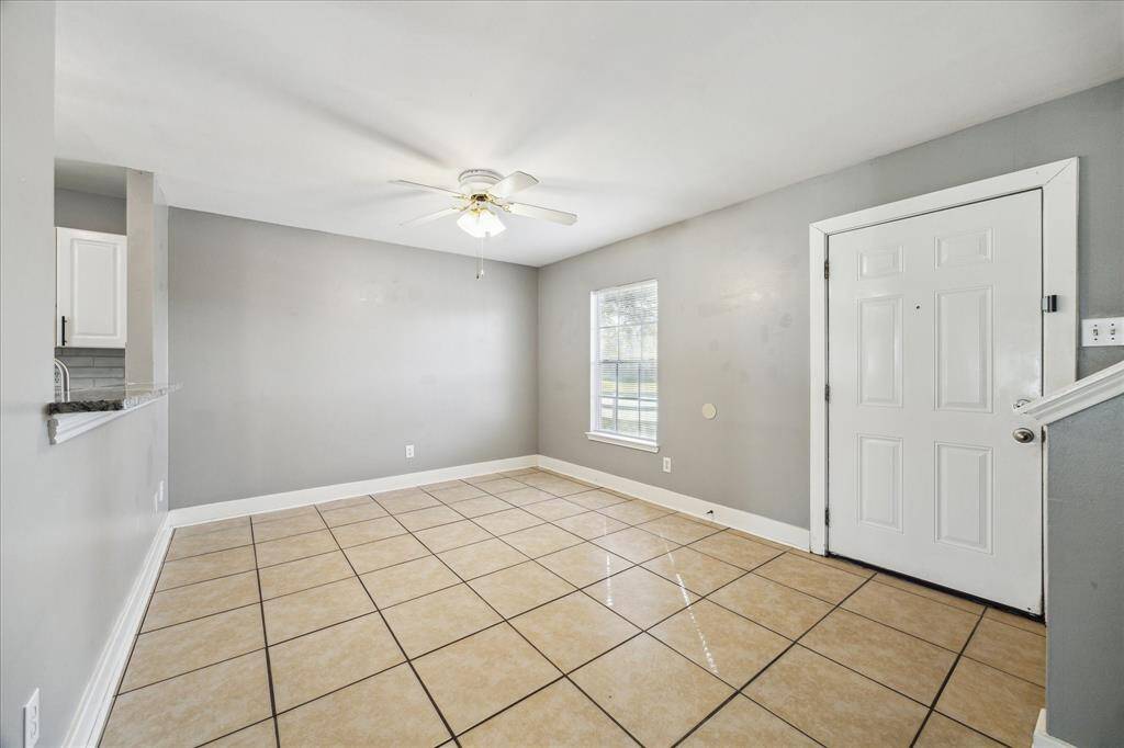 This family room features an open layout with neutral finishes, tile flooring, and a ceiling fan for added comfort. A raised bar separates the kitchen from the family room, providing a convenient space for serving drinks or snacks to guests.