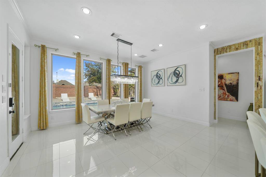 The formal dining room is expansive. and elegant, featuring a grand chandelier that illuminates the space, with a wall of windows offering a picturesque view of the pool, creating a perfect setting for refined gatherings.