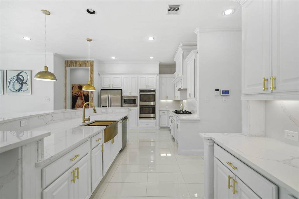The kitchen showcases a spacious quartz waterfall island with sleek, polished edges, centered by a luxurious gold farmhouse sink and tap that adds a touch of opulence to the modern design.