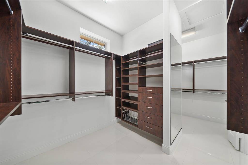 The custom designed His and Hers closets offer abundant storage space with organized shelving and hanging areas, all set against polished tile floors that add a touch of elegance to these spacious, personalized retreats.