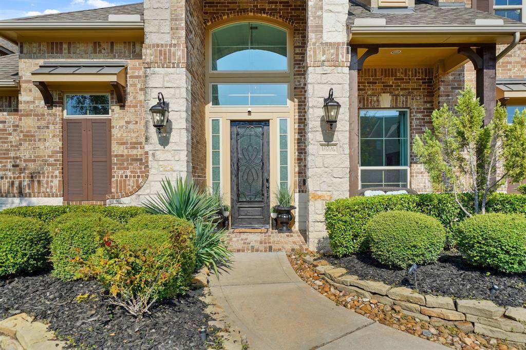 The entrance features a tall, covered patio framed by stately columns, with lush green shrubs on either side, leading to an elegant doorway that exudes a welcoming yet refined charm.