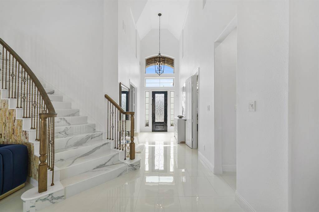 The wrought iron stairway curves gracefully along an accent wall, its intricate detailing complemented by polished tiles that reflect its elegance, adding a striking focal point to the luxurious entryway.