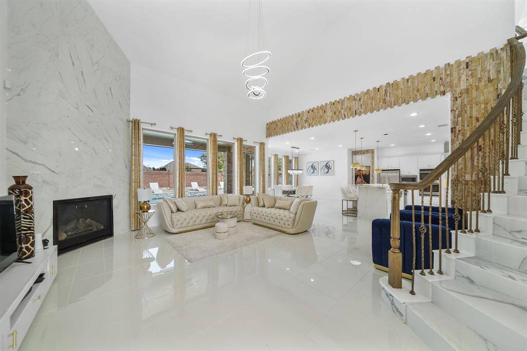 The Family room features tall ceilings with a sparkling chandelier, polished tiles that enhance the rooms elegance, a wall of windows overlooking the pool, and an accent wall with a stylish fireplace as its focal point.