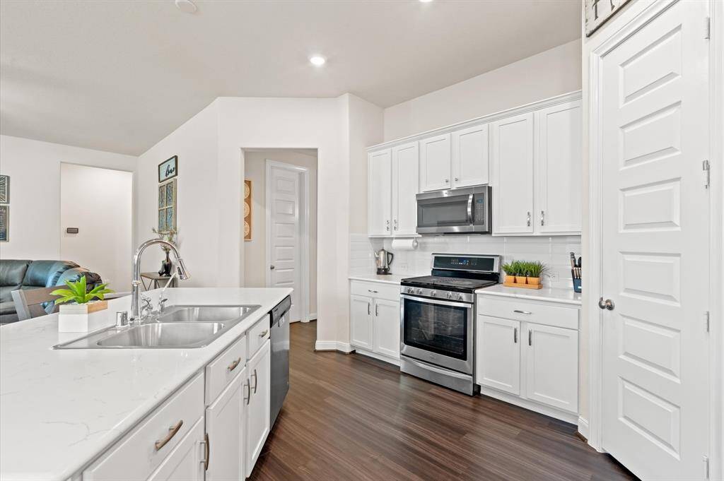 Recessed lighting highlights this classic kitchen with exquisite countertops, a gas range and oven, stainless steel appliances, and a convenient pantry.