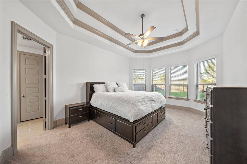 The first-floor primary suite impresses with tray ceilings, wainscoting, and a lavish ensuite bath with dual vanities, a soaking tub, and a glass-enclosed shower. The tall bay windows fill the space with natural light while providing refreshing outdoor views.