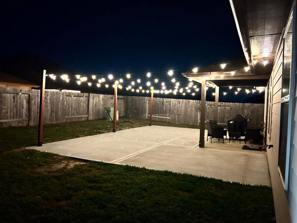 Expansive backyard featuring an extended concrete patio, providing more space to enjoy the outdoors with less lawn maintenance. The patio is enhanced with beautiful lighting, creating a cozy and inviting atmosphere—perfect for gatherings and celebrations.