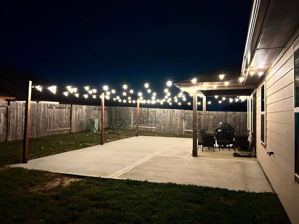 Expansive backyard featuring an extended concrete patio, providing more space to enjoy the outdoors with less lawn maintenance. The patio is enhanced with beautiful lighting, creating a cozy and inviting atmosphere—perfect for gatherings and celebrations.