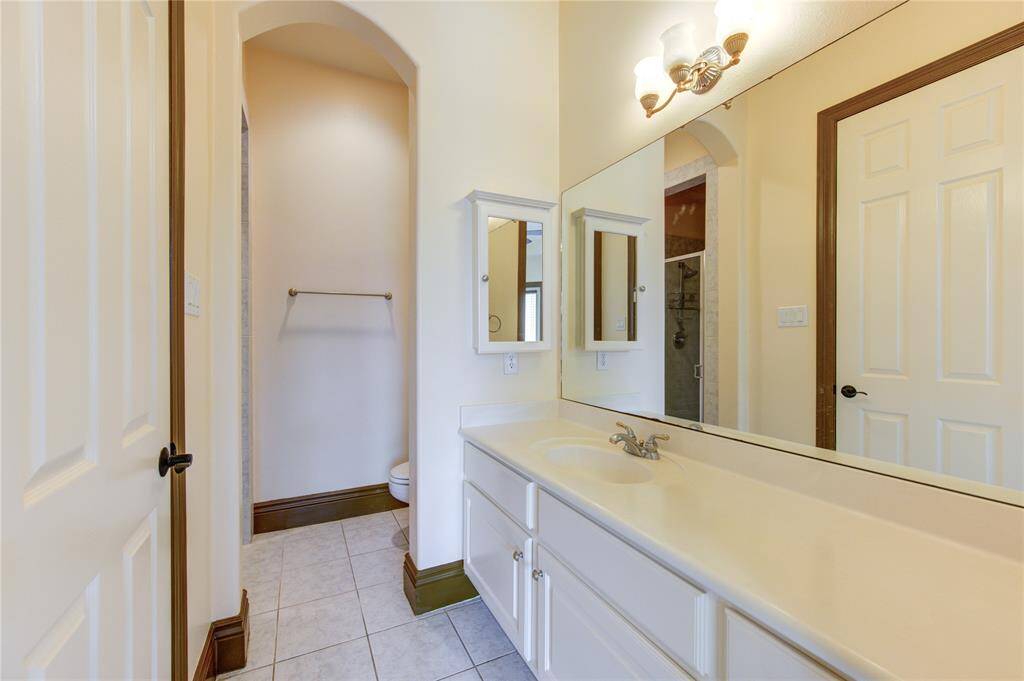 This is an elegant, open-plan living space featuring high ceilings with crown molding, a fireplace with a classic mantelpiece, and large windows for ample natural light. The room flows seamlessly into a well-appointed kitchen with bar seating (virtually staged).