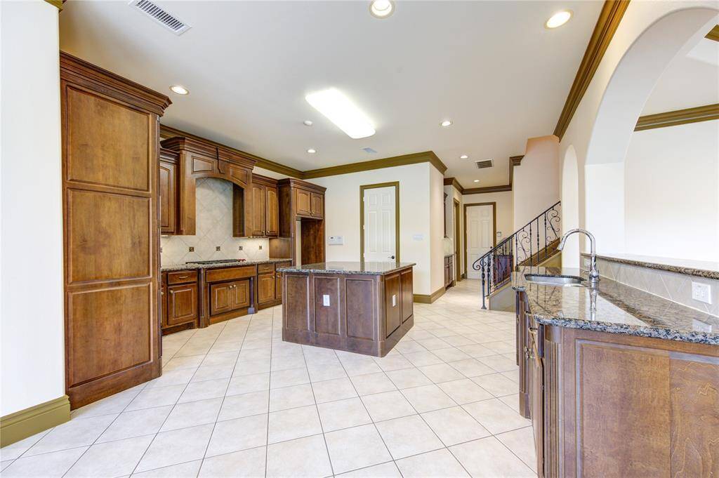 This photo showcases a bright, spacious room with large windows offering a view of a pool and landscaped backyard. The room features tile flooring, crown molding, and a pendant light fixture, creating an inviting atmosphere. An adjoining room with a fireplace is visible through an arched opening.