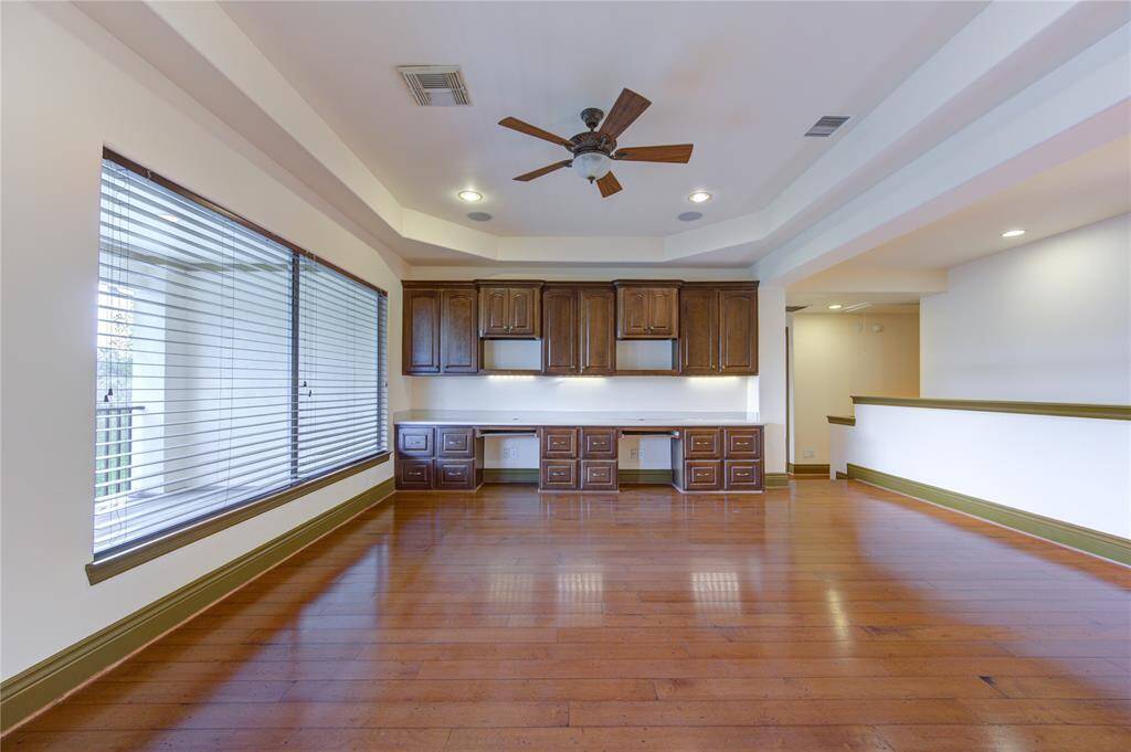 Spacious Primary bedroom with hardwood floors, crown molding, and a tray ceiling with a ceiling fan. It features a large window for natural light and a double door entry to an adjoining room.