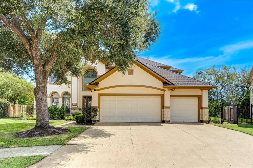 This is a two-story, traditional style home with a large tree in the front yard, arched windows, and a three-car attached garage.