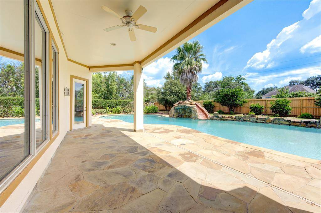 This is a luxurious backyard with a curved swimming pool and a rock waterfall feature, surrounded by a well-maintained garden and privacy fence. The house has a spacious patio area with a view of the pool.