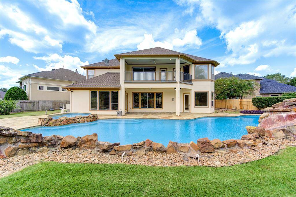 This is an aerial view of a spacious, single-family home with a large, uniquely shaped 75 foot swimming pool and generous backyard space, situated in a suburban neighborhood with ample greenery.