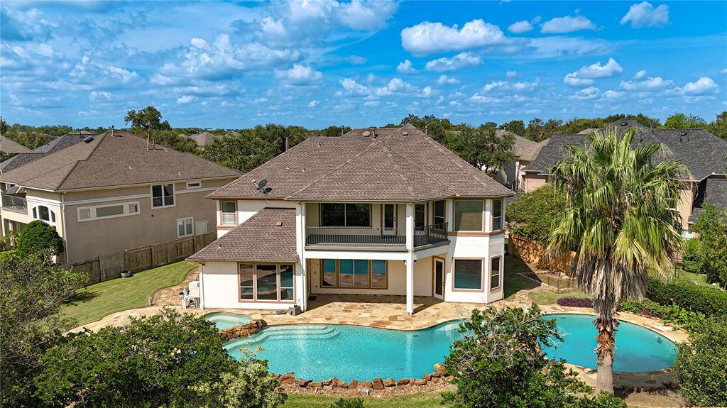 This aerial photo shows a two-story residential property with a sizable, curvaceous backyard swimming pool, well-maintained landscaping, and a generous lawn area, nestled in a suburban neighborhood with similar upscale homes.