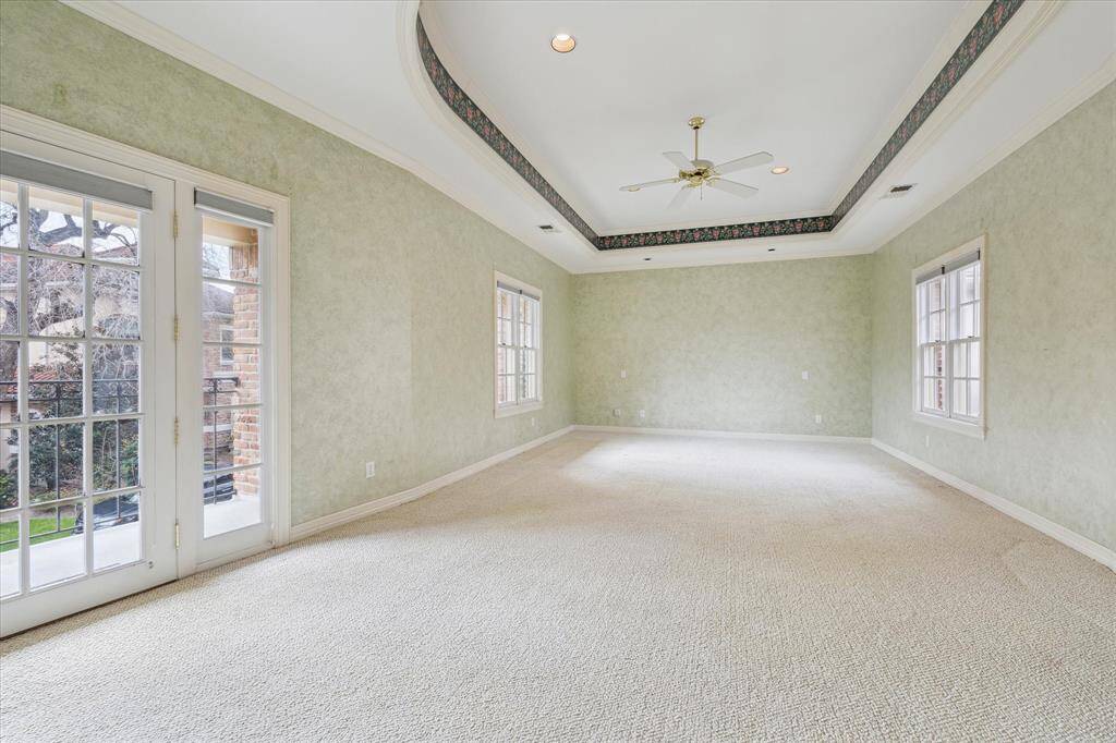 Light-filled second floor primary bedroom with tray  ceiling, has room for large scale furniture, seating area. French door leads to balcony that spans across the entire front of the home