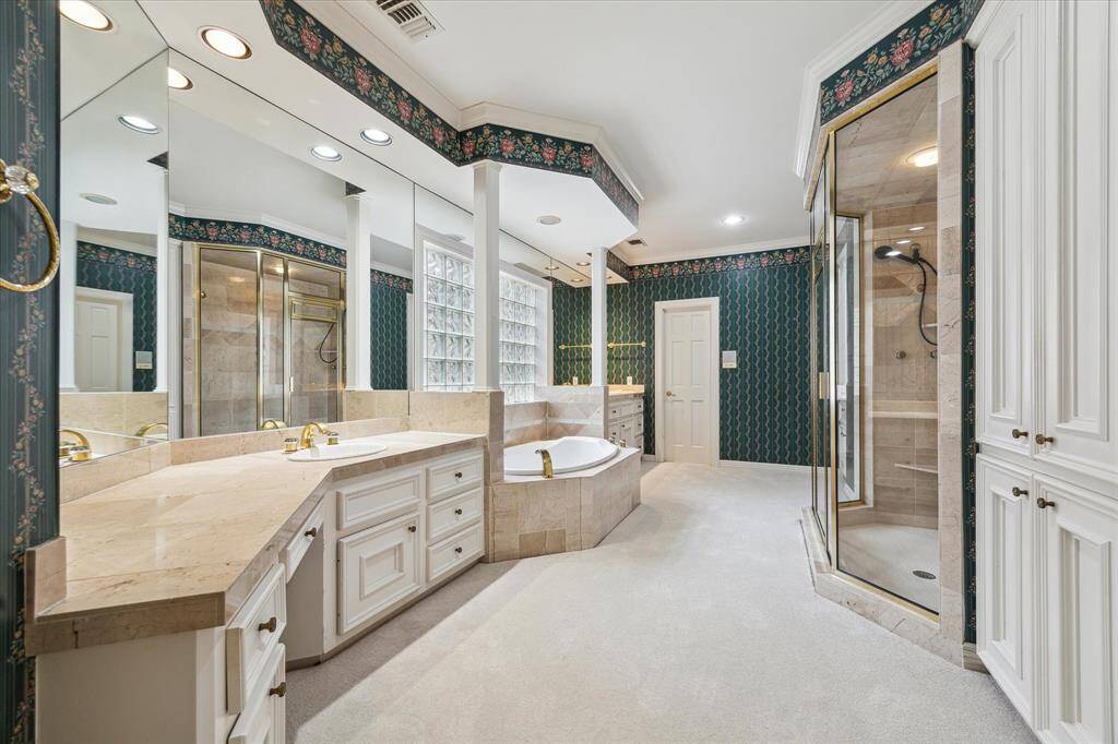 Primary bath area with his and her vanities. soaking tub, oversized shower with dual showerheads.   White marble tile is underneath the carpet.